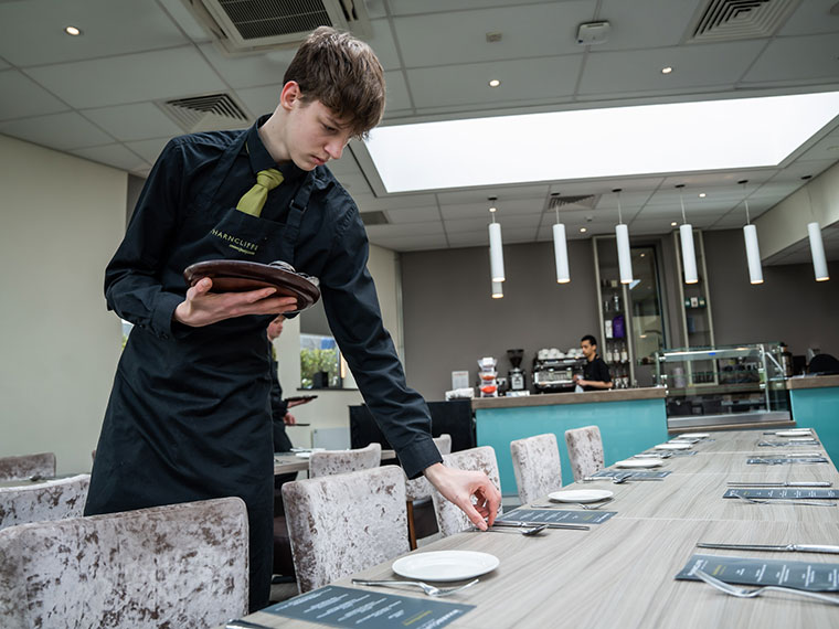 A hospitality student laying a table at The Wharncliffe Restaurant