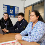 Three adult learners sat at a desk with a laptop in front of them