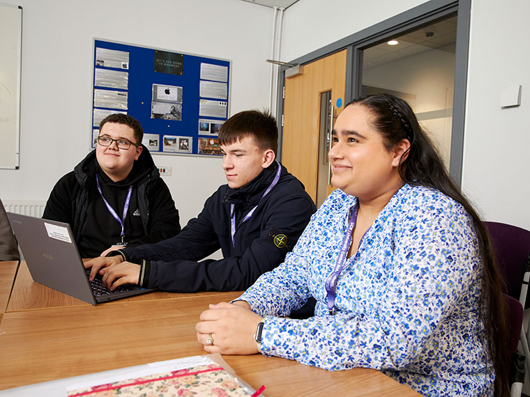 Three adult learners sat at a desk with a laptop in front of them