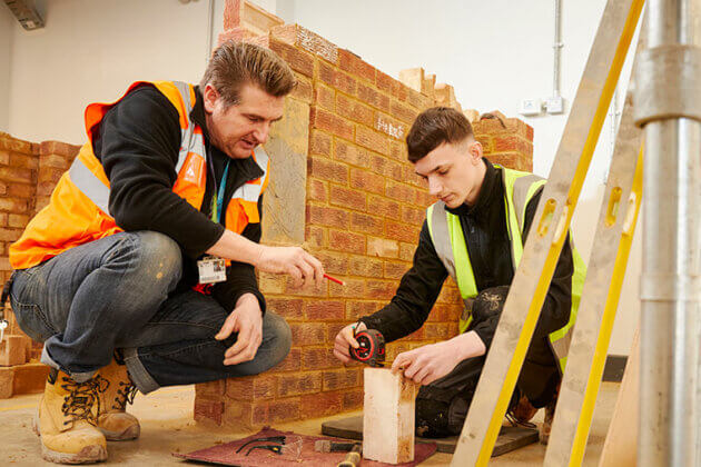 A tutor supporting a bricklaying student with their work