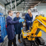 A tutor teaching two students, one student is sat on a small JCB