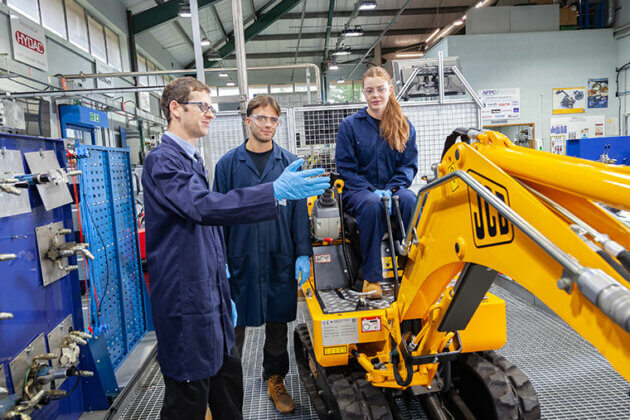 A tutor teaching two students, one student is sat on a small JCB