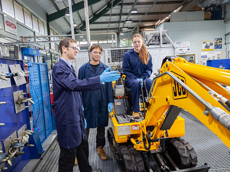 A tutor teaching two students, one student is sat on a small JCB