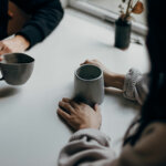 Two people sat acroos from each other at a table holding a hot drink each