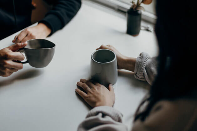 Two people sat acroos from each other at a table holding a hot drink each