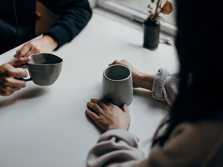 Two people sat acroos from each other at a table holding a hot drink each