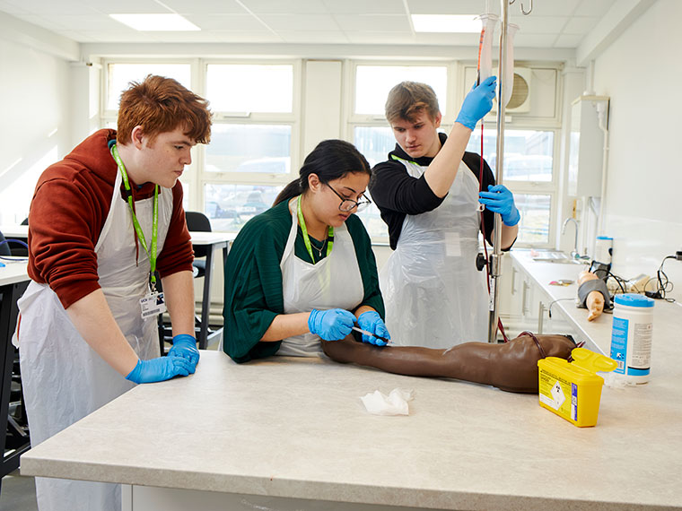 Three students in the health suite practising giving an injection on a fake arm