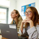 Two students sat side by side at a desk with their laptops open