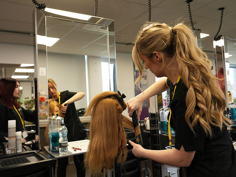 A hairdressing student stood in front of a mirror working on a hairstyle