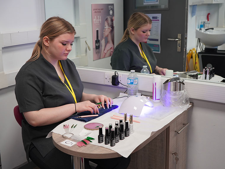 Someone sat behind a desk with nail equipment and nail varnishes in front of them