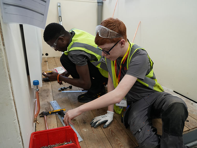 Two people sat on the floor working on piping