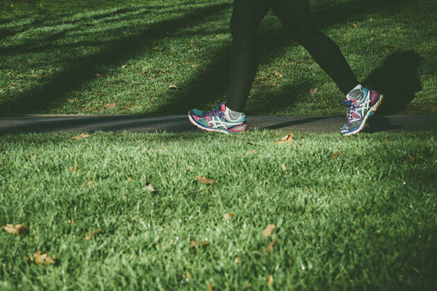 Someone's feet, wearing trainers, walking on a path next to grass