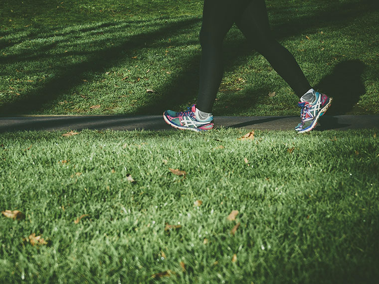 Someone's feet, wearing trainers, walking on a path next to grass