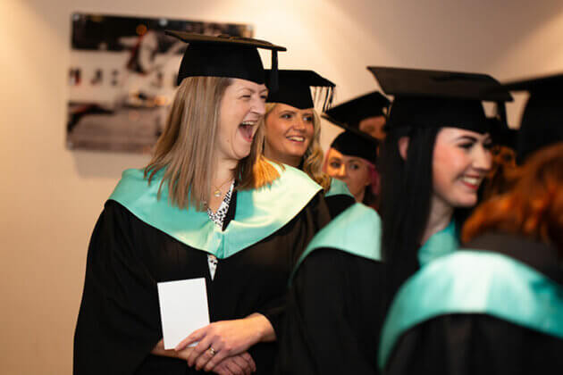 Graduands lining up ready to enter the ceremony room, one person with a big smile