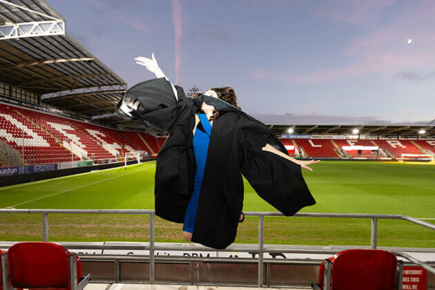A graduate jumping off the ground throwing their hat in the air