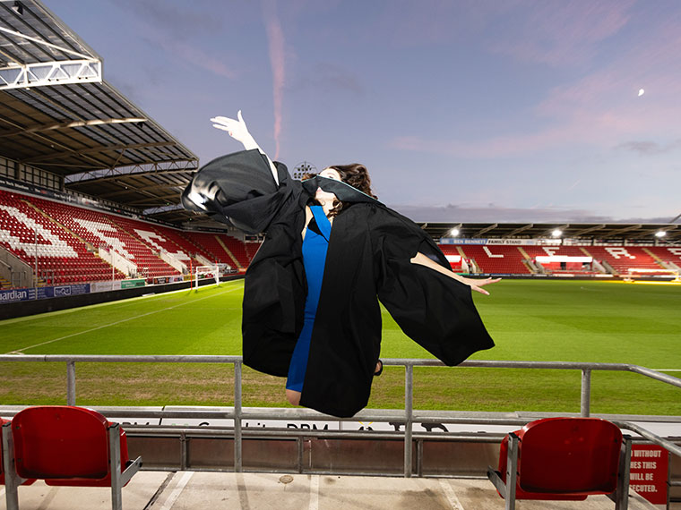 A graduate jumping off the ground throwing their hat in the air