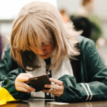 A person sat at a desk looking down at their mobile phone