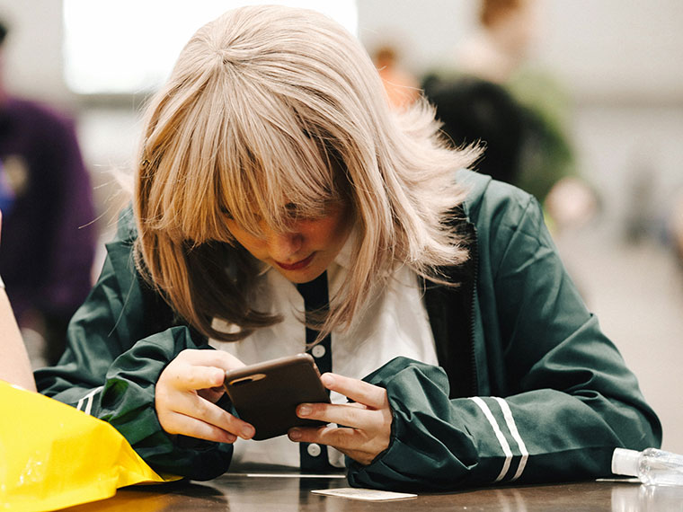 A person sat at a desk looking down at their mobile phone