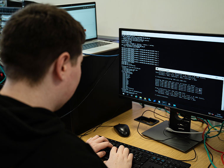 A student sat at a desk typing code into a computer