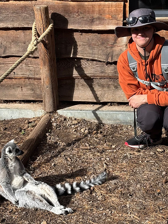 UCR Animal Management student Finn smiling crouching next to an animal