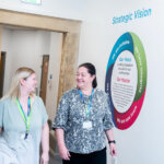 Two members of staff walking down a corridor together smiling