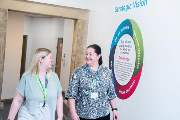 Two members of staff walking down a corridor together smiling