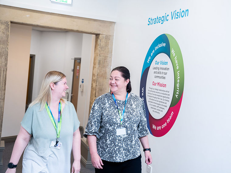 Two members of staff walking down a corridor together smiling
