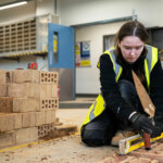 A student knelt down checking brick with a spirit level
