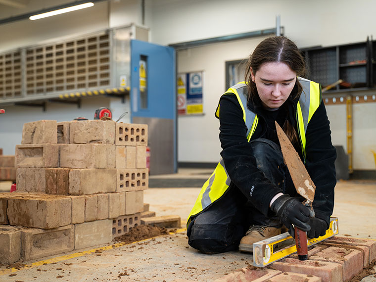 A student knelt down checking brick with a spirit level