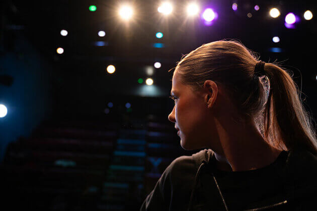 A close up of the side of someone's head as they look out towards the audience and the lights