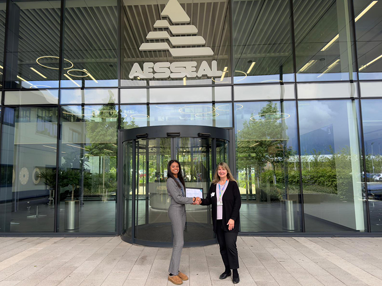 Two ladies shaking hands stood outside a glass building with the Aesseal logo above them on the glass