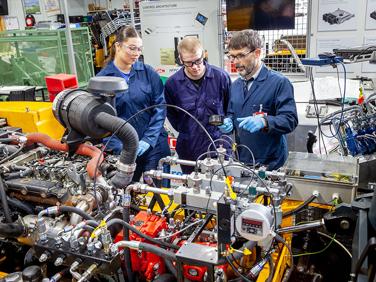 A tutor speaking to two students next to machinery