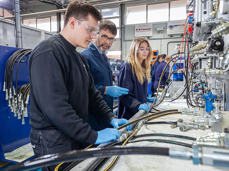 A tutor speaking to two students next to machinery