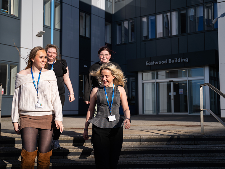 Four students smiling walking down the steps outside Rotherham College's Eastwood Building