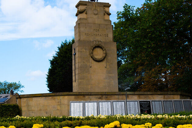 The Rotherham Remembrance Cenotaph in Clifton Park, yellow flowers at the foot of it