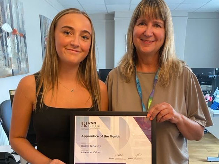 Two females stood together holding a framed certificate between them