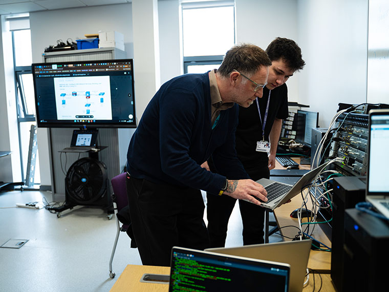 A lecturer and student stood in a classroom both looking at the same laptop