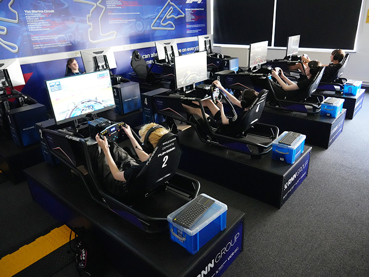 Four people each using an esports F! simulator, holding a steering wheel looking at a screen in front of them