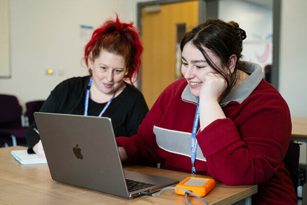 Two people sat together at a table both looking at the same laptop