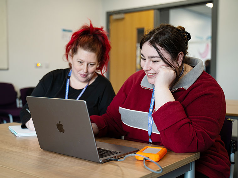 Two people sat together at a table both looking at the same laptop