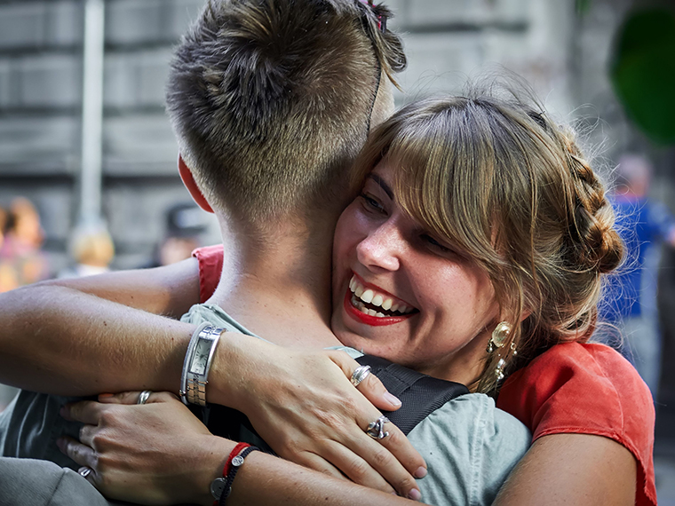 A smiling female in a red tee shirt hugging a male in a gray tee shirt