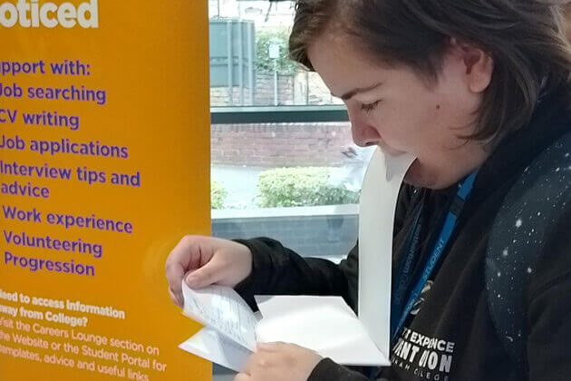 Someone holding a piece of paper in their mouth whilst looking down at other sheet of paper in their hands