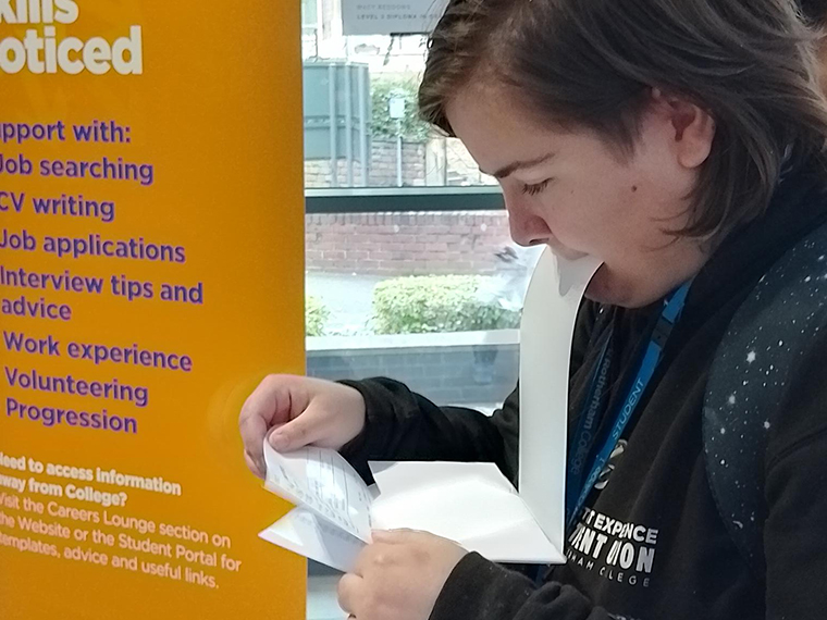 Someone holding a piece of paper in their mouth whilst looking down at other sheet of paper in their hands
