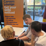 Three people seated and chatting, a pull up banner in the background that reads 'Careers Lounge Get your skills noticed'
