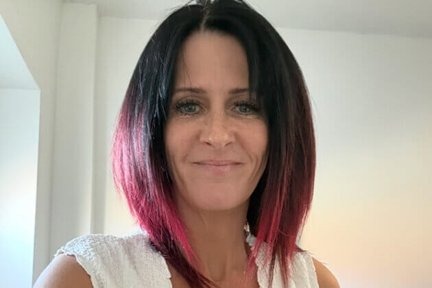 A head and shoulders photo of a smiing lady with black and red hair and a white top