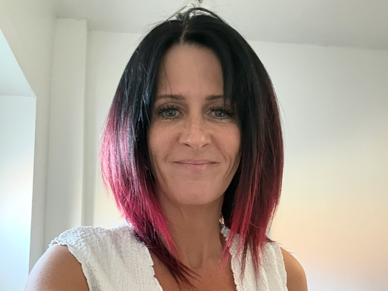 A head and shoulders photo of a smiing lady with black and red hair and a white top