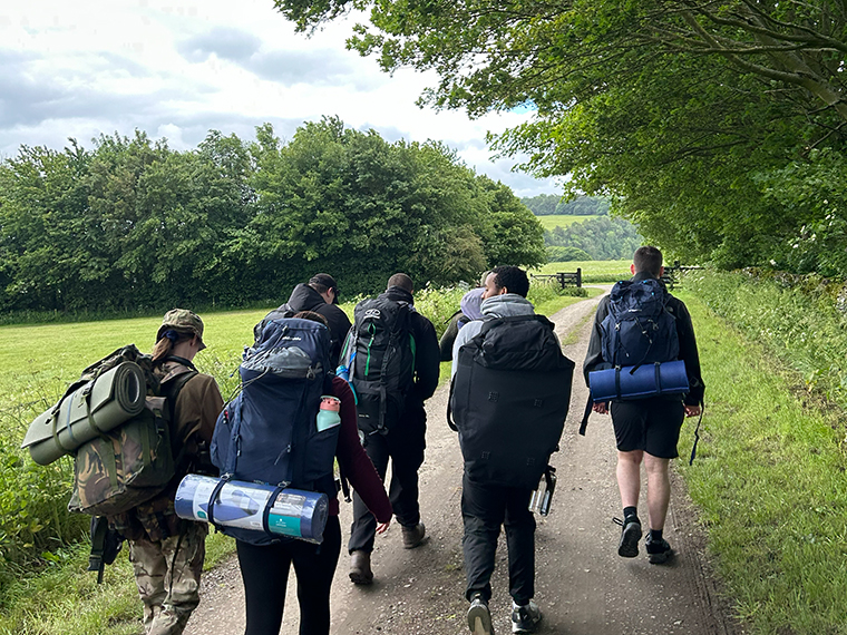 A group of people holding backpacks walking down a path with trees either side