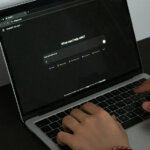 Hands typing on a laptop 'what can I help with?' is on the screen