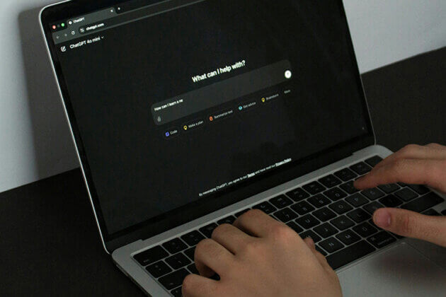 Hands typing on a laptop 'what can I help with?' is on the screen