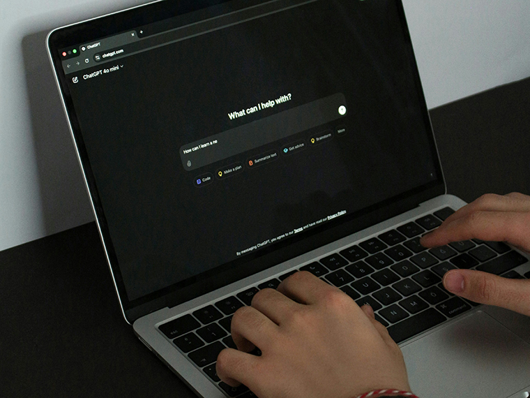 Hands typing on a laptop 'what can I help with?' is on the screen